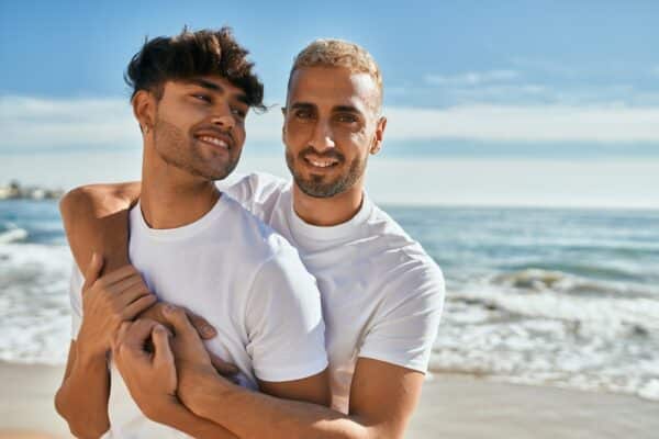 Young gay couple smiling happy hugging at the beach.